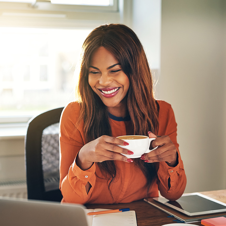 Black woman with a cup of coffee at a laptop, having individual therapy online in California, Oregon, and Washington